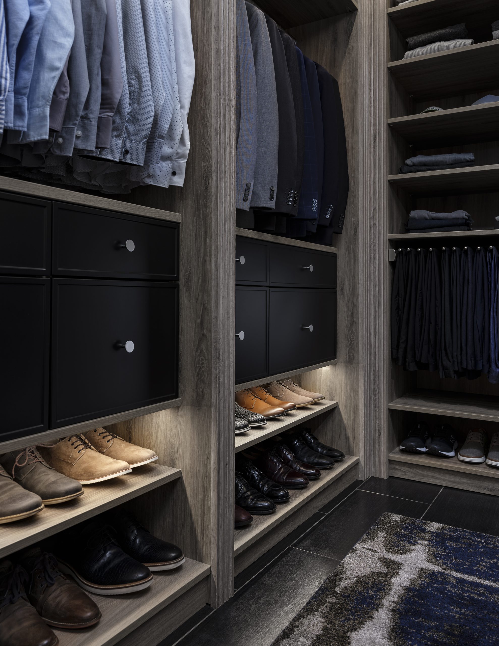 Closeup view of a custom closet system with men's dress shirts and shoes neatly displayed on dark wood shelves. 